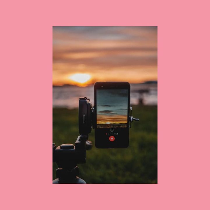 Älypuhelin jalustalla tallentaa UGC-videota auringonlaskusta rannalla.
